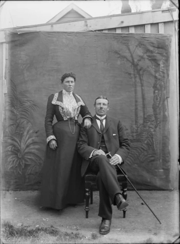 Image: Unidentified couple outdoors, with a painted studio backdrop, shows man holding a cane, probably Christchurch district