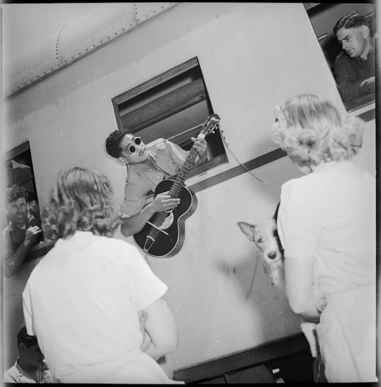 Image: Blind Maori soldier repatriated from Italy playing guitar out of railway carriage window at Alexandria, World War II - Photograph taken by G R Bull