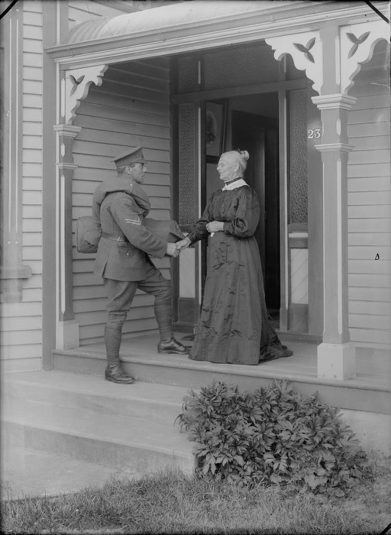 Image: Outdoors on a veranda of a wooden house, a farewell between an unidentified elderly mother with her older World War I Corporal Soldier son carrying his coat and kit bag, probably Christchurch region