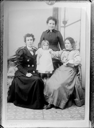 Image: Studio unidentified portrait of three women with a young girl, two women [sisters?] with double breasted jacket and a lace trim pleated blouse with bow ties sitting in front with an older woman [mother?] in a [Salvation Army?] dress standing behind, location unknown