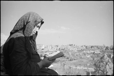 Image: Italian peasant woman reading a bible with the ruins of Orsogna in background, Italy, World War II - Photograph taken by George Kaye