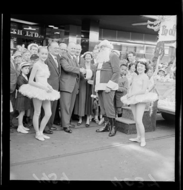 Image: Mr R G Button with a crowd of onlookers and two young ballet dancers, welcoming Father Christmas to Cuba Street, Wellington