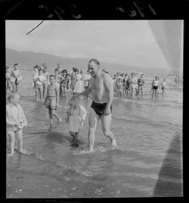 Image: An unidentified man completing the Somes Island Petone swim being greeted on Petone Beach by his young daughters with children looking on, Wellington City