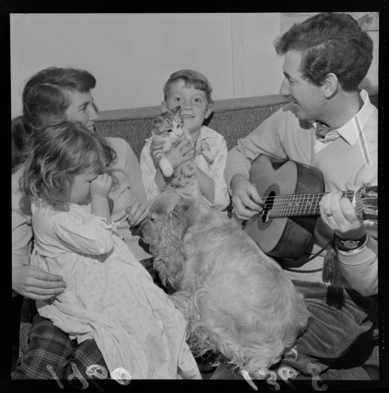 Image: Folk musician, theologian and writer Peter Cape with guitar and family within their home at an unknown location, probably Wellington Region