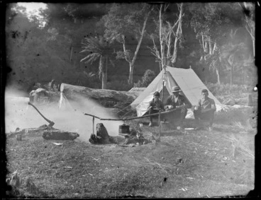 Image: Edgar and Owen Williams with unidentified man sitting outside a tent and eating a meal with the campfire in front, Catlins District