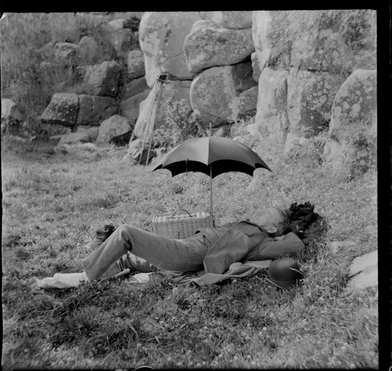 Image: Unidentified man lying on the grass beside picnic basket and umbrella, unknown location