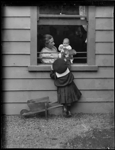 Image: Lydia Williams holding Owen as a baby sitting inside their home, with Edgar outside passing a toy through the window, at 'View Bank', Maitland Street, Dunedin