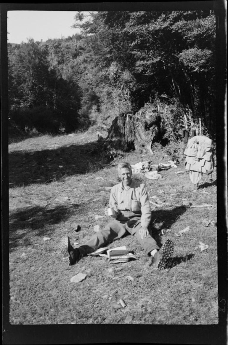 Image: Edgar Williams with a box of Weetbix, drinking tea, on a mountaineering trip, in a grassy clearing, location unidentified