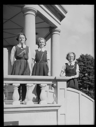 Image: Three unidentified schoolgirls from Westport Technical High School, at a sportsday prizegiving, standing on the platform of a band rotunda, probably West Coast Region