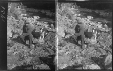 Image: An unidentified man with a dog, boiling a billy over a campfire next to a river, [Franz Josef Glacier, West Coast Region?]