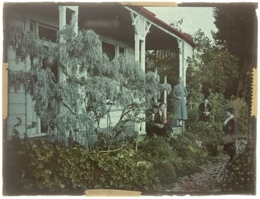 Image: Group of unidentified women and man, standing on a wooden verandah with a wisteria vine in foreground, location unidentified