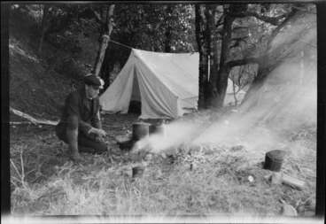 Image: An unidentified man cooking over an open fire at a bush campsite, Mount Torlesse, Canterbury Region