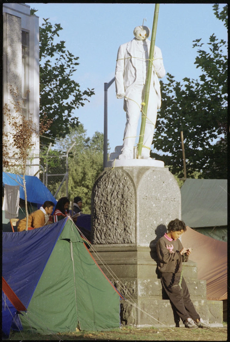 Image: Kia Kingi practising flax plaiting beneath statue of John Ballance, Moutoa Gardens, Wanganui