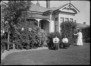 Image: Three unidentified women in a garden, beside a villa with verandah partially visible.