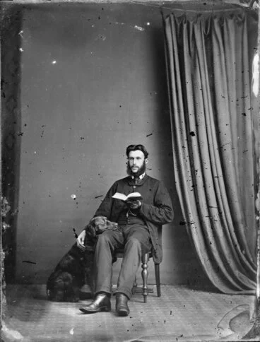 Image: Unidentified man, seated, with a book and his dog