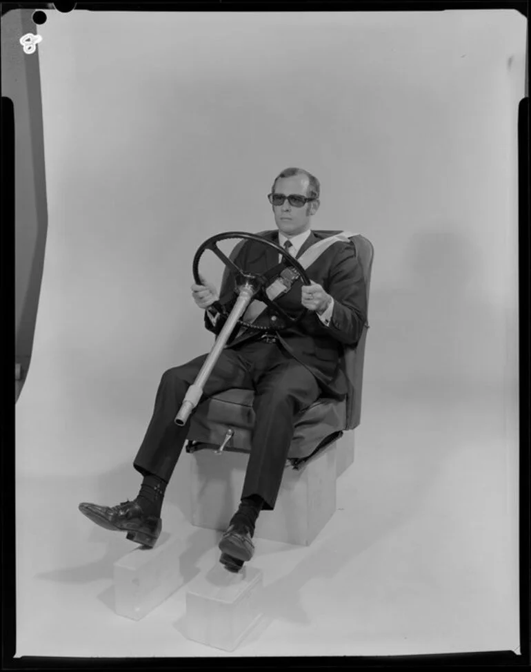 Image: Man in studio sitting in car seat, with steering wheel and seatbelt