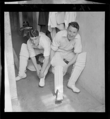 Image: Two unidentified members of a cricket team, putting on leg pads, Basin Reserve, Wellington