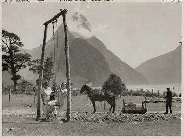 Image: Two unidentified women on a swing, and a man unloading stores, Milford Sound