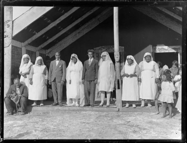 Image: Brides, grooms and Awhina of the Rātana church in front of a meeting house, Korohe marae