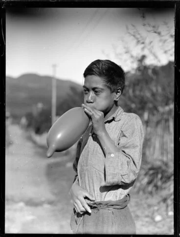 Image: Māori boy, possibly Moetu Otimi, blowing up a balloon, Waikato