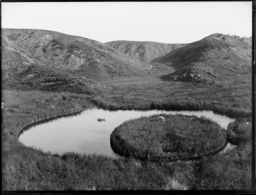Image: A lake with a circular floating island, including two men in a dinghy, Whakaki, Wairoa District
