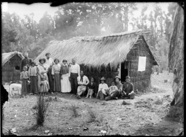 Image: Group of Maori men, women and children with William Williams and Fred Byrne outside a thatched whare, Te Kauri, Otorohanga District