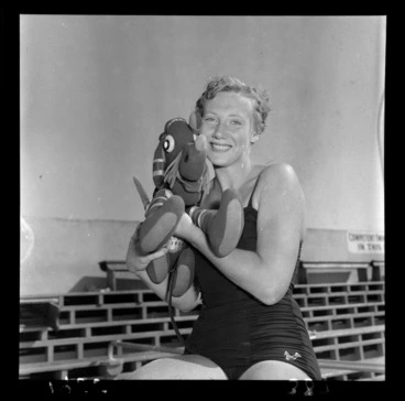 Image: [Swimmer?] Marion Roe sitting in her swimsuit at the poolside holding a stuffed toy elephant