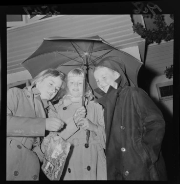 Image: Three unidentified Hutt Valley girls under an umbrella on Guy Fawkes, including a sparkler and bag of fireworks