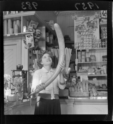 Image: Young woman named Lynn inside a fruit and vegetable shop holding a long narrow vegetable called a java bean