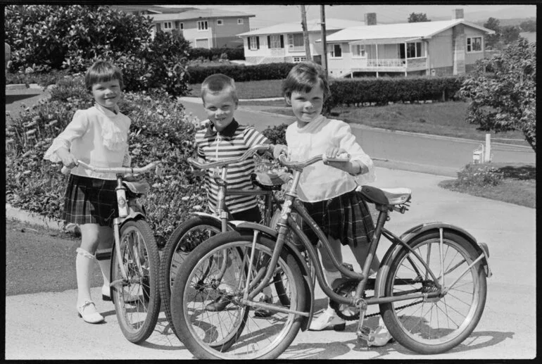 Image: Three children at a family party (?) in the driveway with new (?) bicycles.