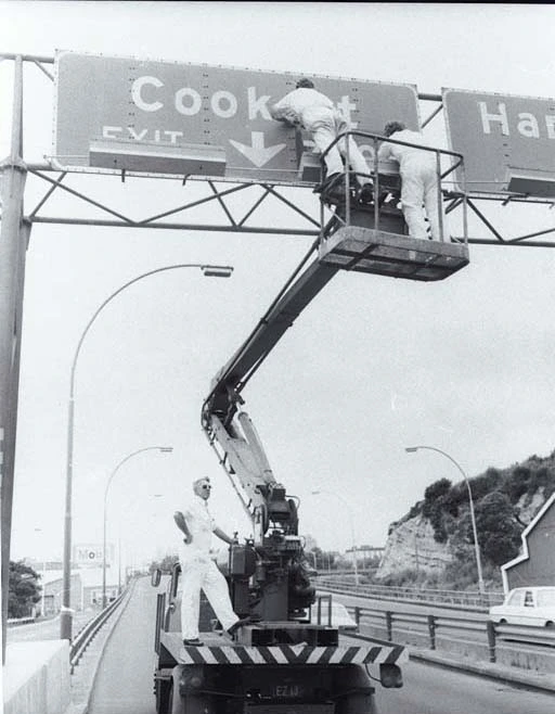 Men working on a Cook Street off-ramp sign on the northern motorway