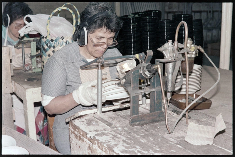 Negative - Worker sitting at mounted machine, holding stack of plates applying colour or similar
