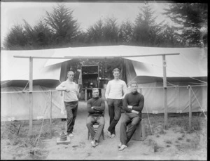 Group of unidentified young men outside a large tent, showing cooking equipment storage area in the background, probably Christchurch district