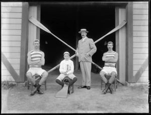 Unidentified members of a rowing team [Avon Rowing Club members?] in an unidentified outdoor location showing two rowers, a boy coxswain and team coach with two oars placed diagonally in the background, probably Christchurch district