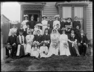 Large wedding group, including bride and bridegroom, best man, and bridesmaids, with other unidentified men, women and children, outside a wooden house, possibly Christchurch district