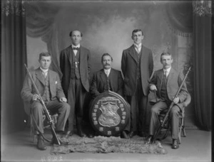 Studio portrait of unidentified members of the South Island Rifle Association members, including two unidentified men holding rifles and shield trophy, probably Christchurch district