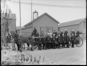 Group of unidentified firemen of the Railway Volunteer Fire Brigade, at an unidentified location, probably Christchurch district, including horse-drawn engine and buildings behind