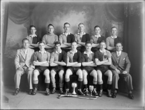 Studio portrait of men's hockey team, unidentified player in uniforms with coaches, with hockey sticks and cups in front, Christchurch