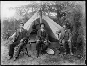 Three unidentified men sitting outside a tent, probably Christchurch district, includes a bicycle and a British flag on the left