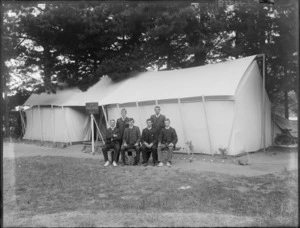 Group of six unidentified young men outside a large tent, with a sign reading 'The Toreador Camp' and an accordian on the ground, probably Christchurch district