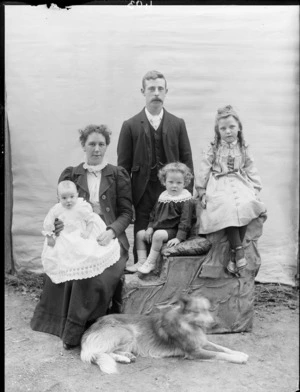 Family group, including a man, woman, and three children, all unidentified, with a dog, standing in front of a plain scrim, possibly Christchurch district