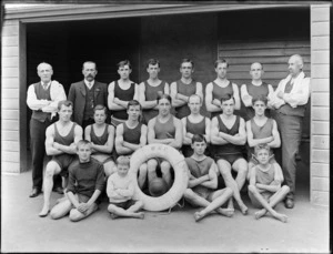 Group of unidentified men and boys wearing swimming costumes, [swimming team? lifeguards?], with a lifesaving ring buoy stamped with the letters WBC, possibly Christchurch district