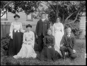 Family group, showing unidentified men and women including one very fashionably dressed young woman with a heart-shaped brooch on the collar of her blouse, in a garden, possibly Christchurch district