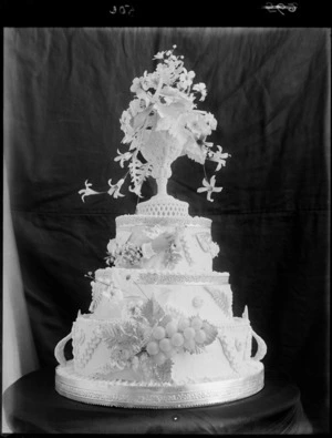 A three-tiered wedding cake, decorated with fruit, flowers and a hand modelled in royal icing