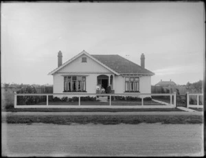 Street view of a wooden bungalow, with two women and a man, all unidentified, standing at entrance, possibly Christchurch district