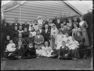 Wedding group portrait in back garden lawn area with house beyond, unidentified bride with long veil and groom with extended family, children and babies in front, probably Christchurch region