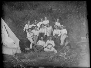 Group of unidentified young men, wearing naval shirts, [boy scouts?], sitting on a grass bank, at a campsite, possibly Christchurch district