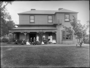 A group of unidentified people, two women and 14 children, on the porch and lawn in front of the house, showing some of the children sitting on the porch and the lawn, with the two women and the girl standing on the porch and the boys standing on the lawn, possibly Christchurch district