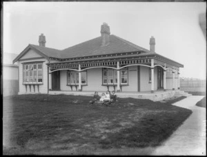 Four unidentified children sitting on the lawn in front of the house, possibly Christchurch district, showing the sign Lindisfarne on the house