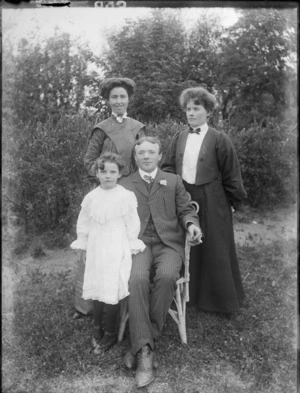 Members of an unidentified family, showing the man sitting on a chair, in the garden, probably Christchurch district